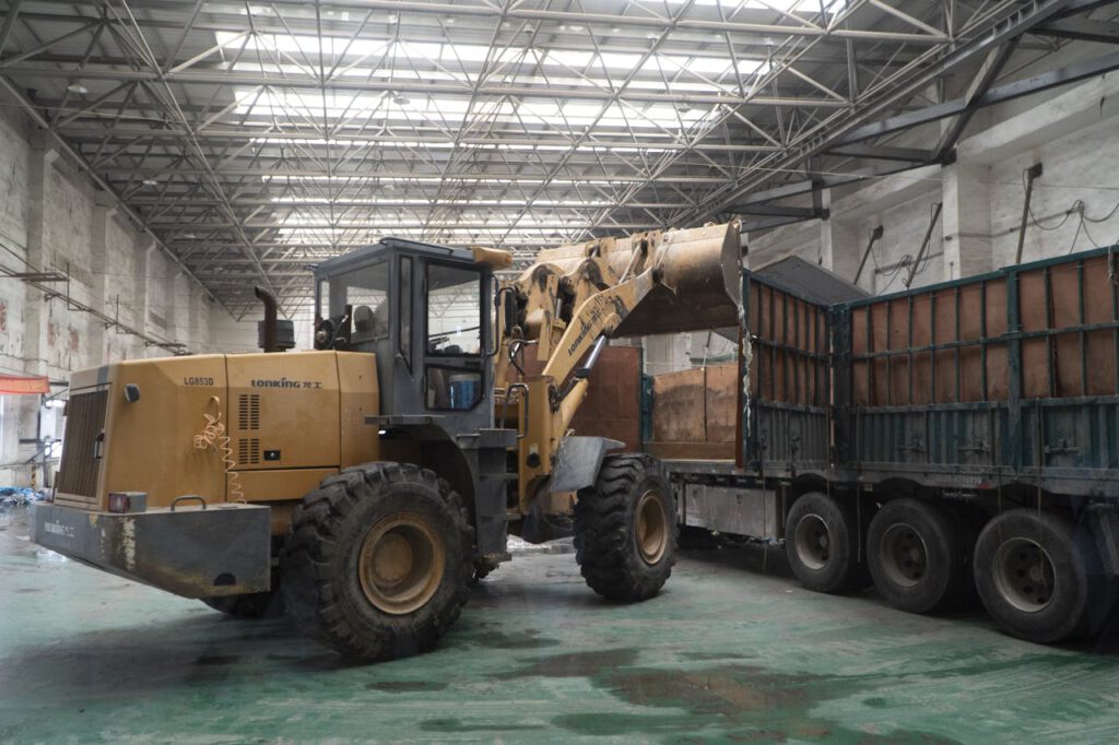 Heavy-duty loader transferring materials onto a truck inside a large warehouse.