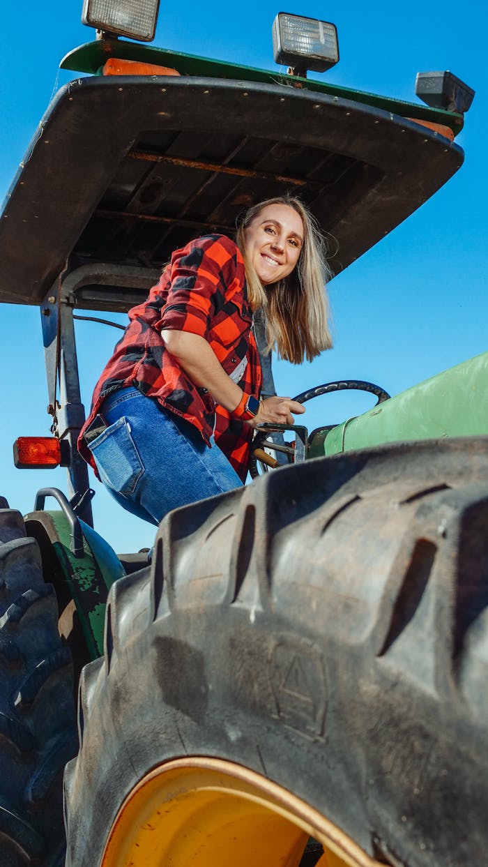 A woman confidently navigating a tractor on a sunny day, showcasing empowerment in farming.